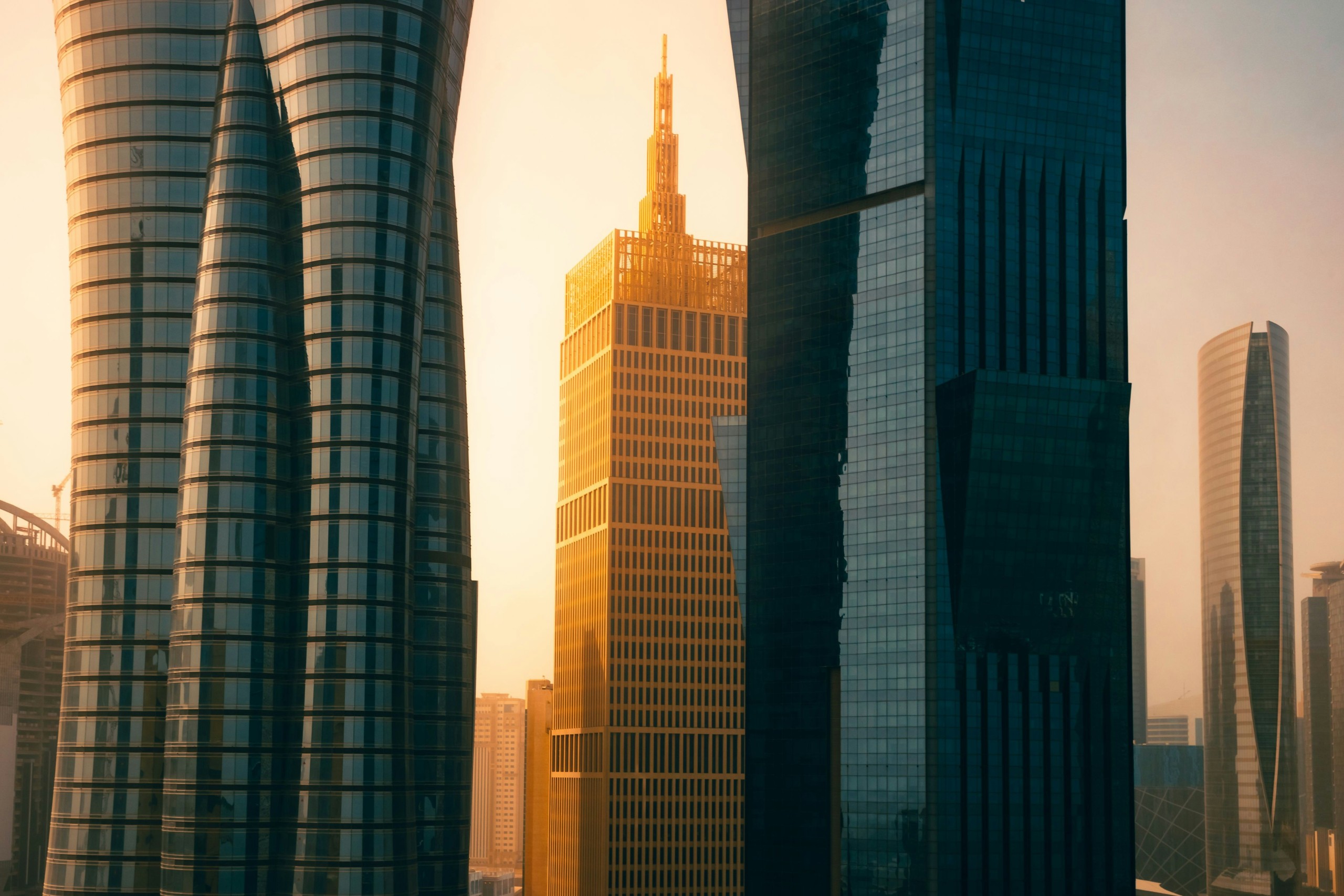 Tall modern skyscrapers in a city at sunset, with one central golden building surrounded by glass and steel high-rises.