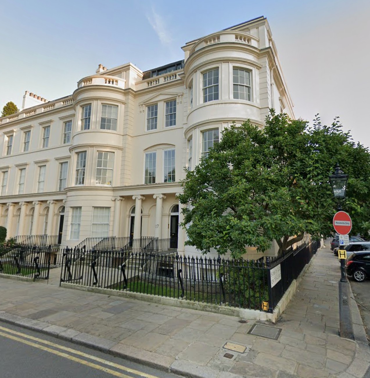 A large, cream-coloured Georgian building with rounded bay windows, black railings, and a tree out front, situated on a corner in an urban setting.