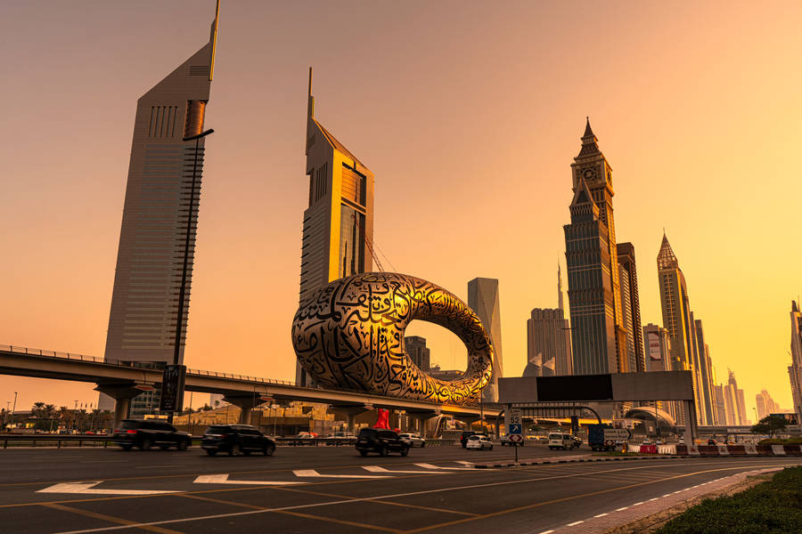 A cityscape at sunset shows the Museum of the Future, a torus-shaped building with Arabic calligraphy, surrounded by skyscrapers and a road with moving cars in Dubai, UAE.